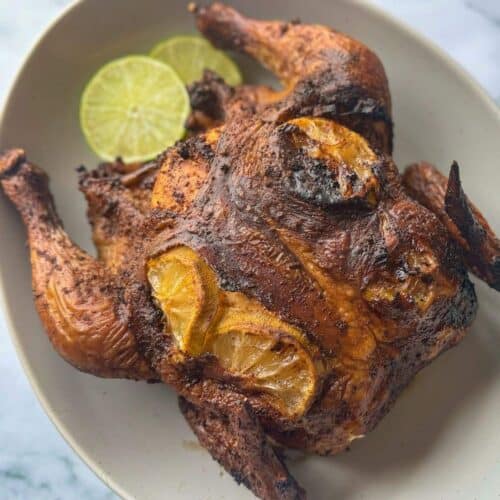 This is a smoked whole chicken with lime slices on a gray platter.