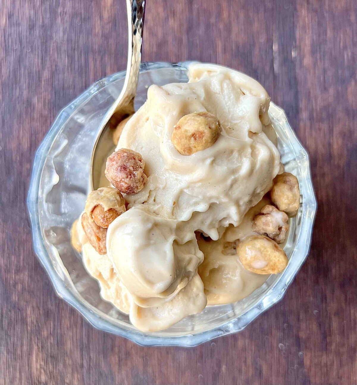 peanut butter ice cream scoops topped with peanuts in glass dish on wooden table