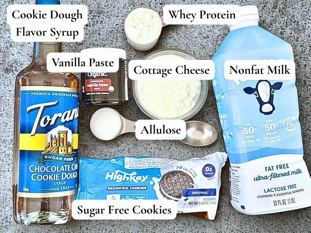 Ninja Creami recipe ingredients such as sugar free syrup, sandwich cookies, milk, and protein powder on a gray background.