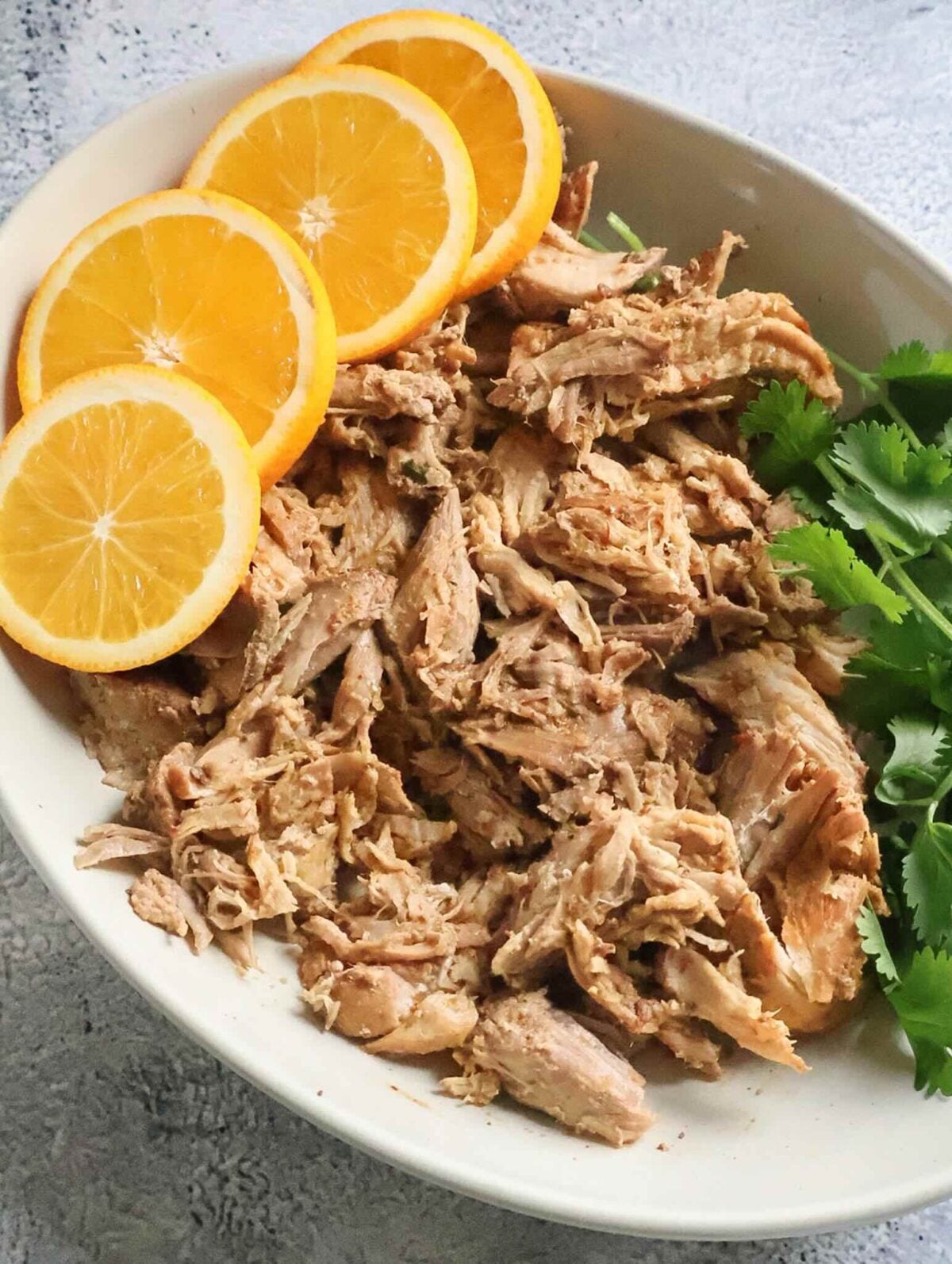 A platter of shredded smoked pork with orange slices and cilantro.