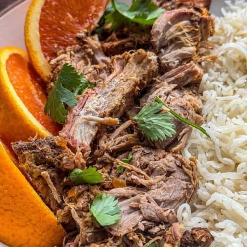 bowl of shredded smoked boneless pork roast recipe with orange slices, cilatro, and white rice