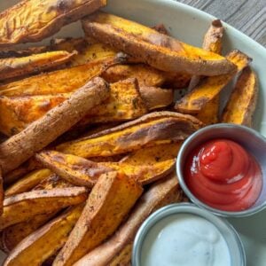 This is a platter of air fried sweet potato wedges with ketchup and ranch in dipping cups.