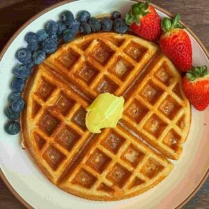 This is a kodiak cakes protein waffle with butter & syrup with fruit on a white plate.