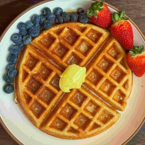 This is a kodiak cakes protein waffle with butter & syrup with fruit on a white plate.