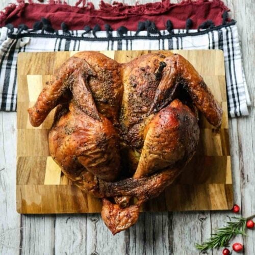 Smoked spatchcocked turkey on a cutting board with cloth napkins, rosemary, and cranberries on wooden background.