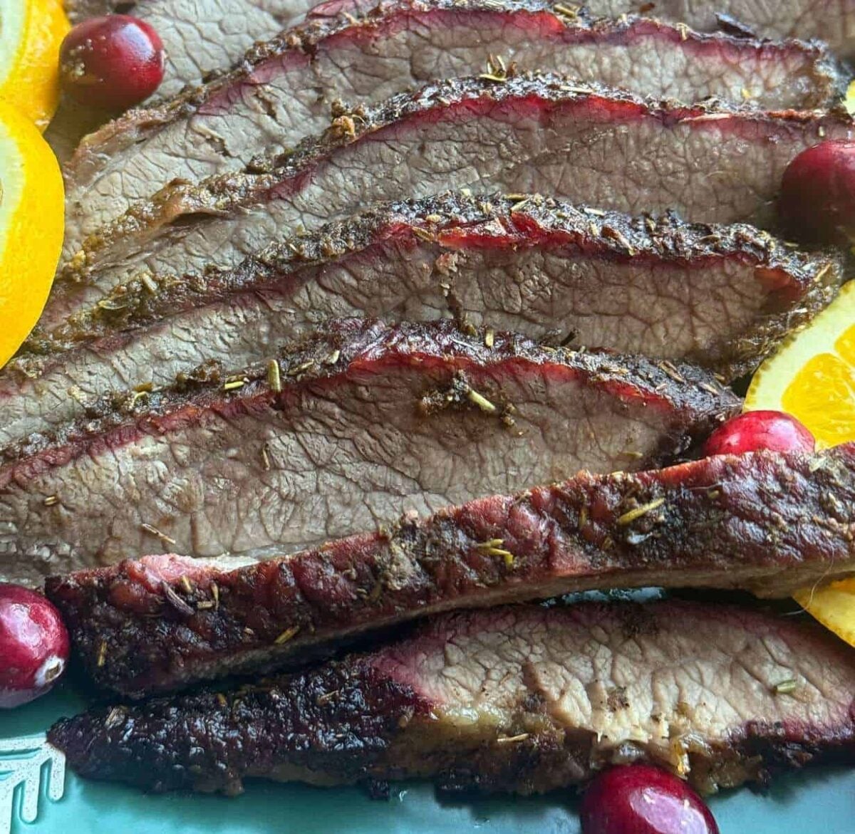 Brisket slices showing smoke ring with cranberries and orange slices.
