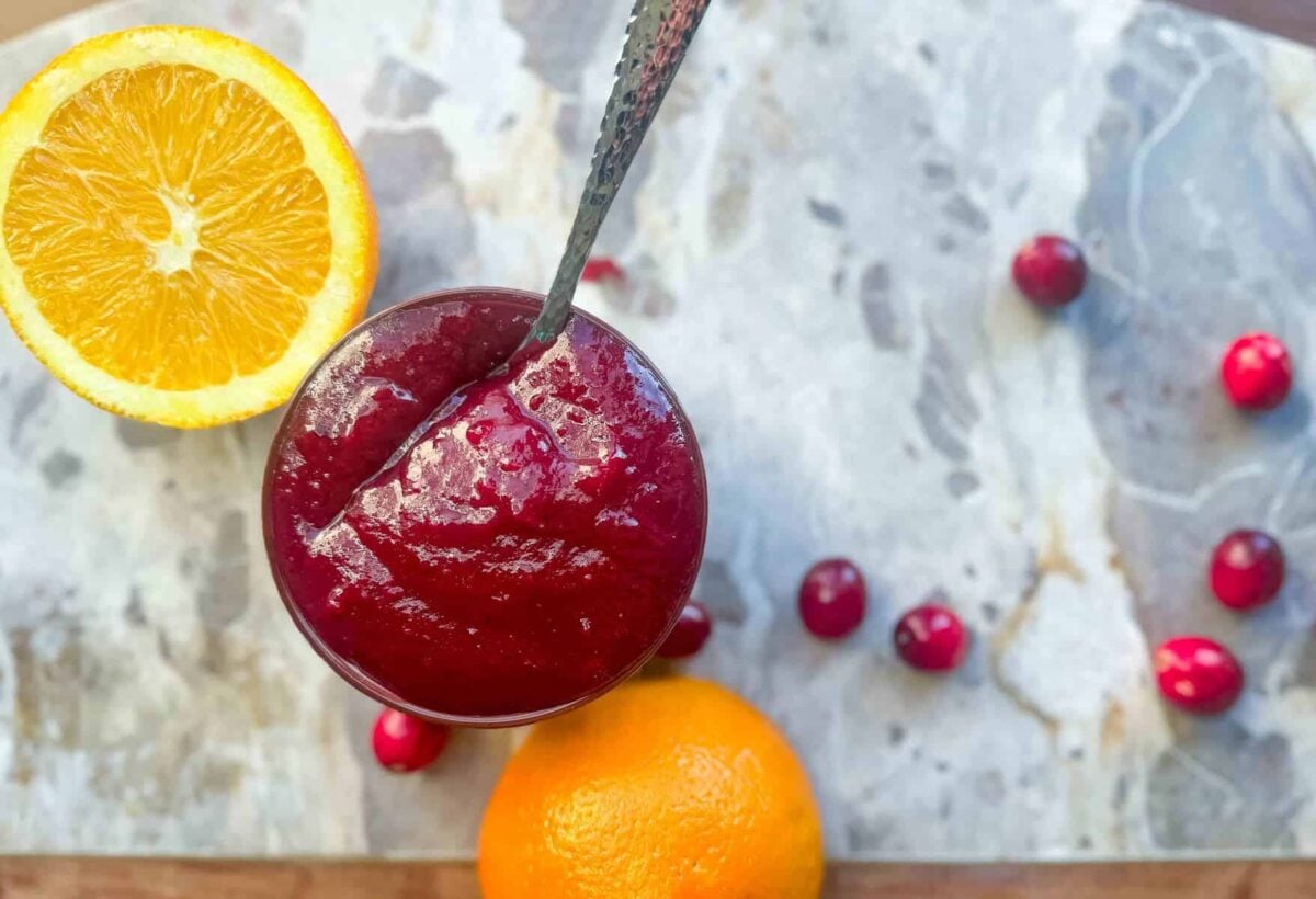 close up of cranberry bbq sauce in dish on marble slab with oranges and cranberries