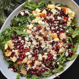 winter kale salad with pomegrantes and apples in platter with winter foliage in corner