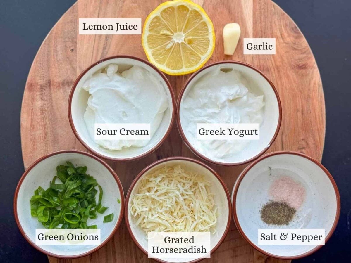 Small bowls of ingredients for yogurt horseradish sauce on a wooden backdrop.
