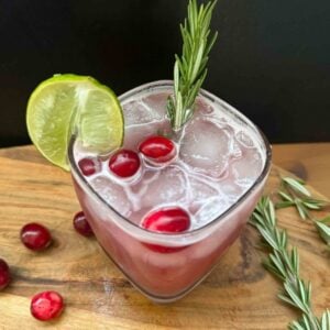 cranberry ginger mocktail on wooden board with black background, cranberry & rosemary garnish