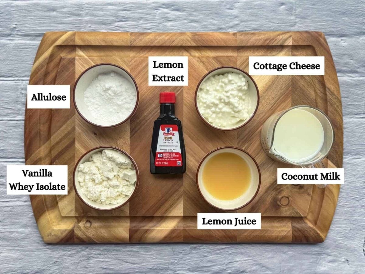 lemon ice cream ingredients on wooden board including protein powder, allulose, lemon extract & juice, coconut milk, cottage cheese
