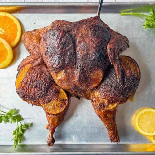 Smoked spatchcocked chicken on a sheet pan with citrus and parsley garnishes.