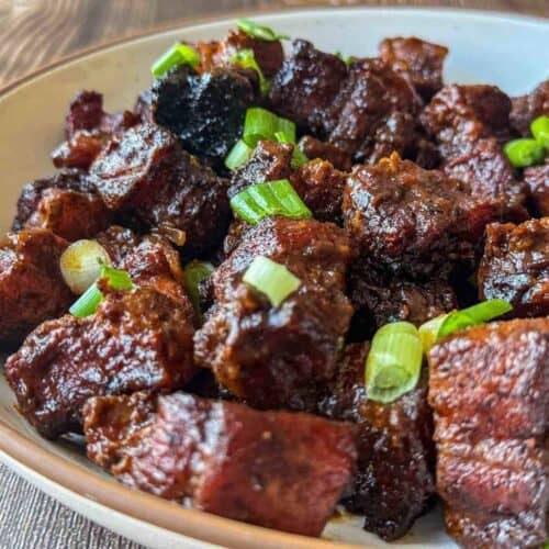 traeger pork belly burnt ends garnished with green onion in white bowl.