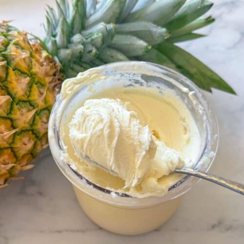 This is a ninja creami pint container with dole whip next to a pineapple with a spoon taking out a big bite.