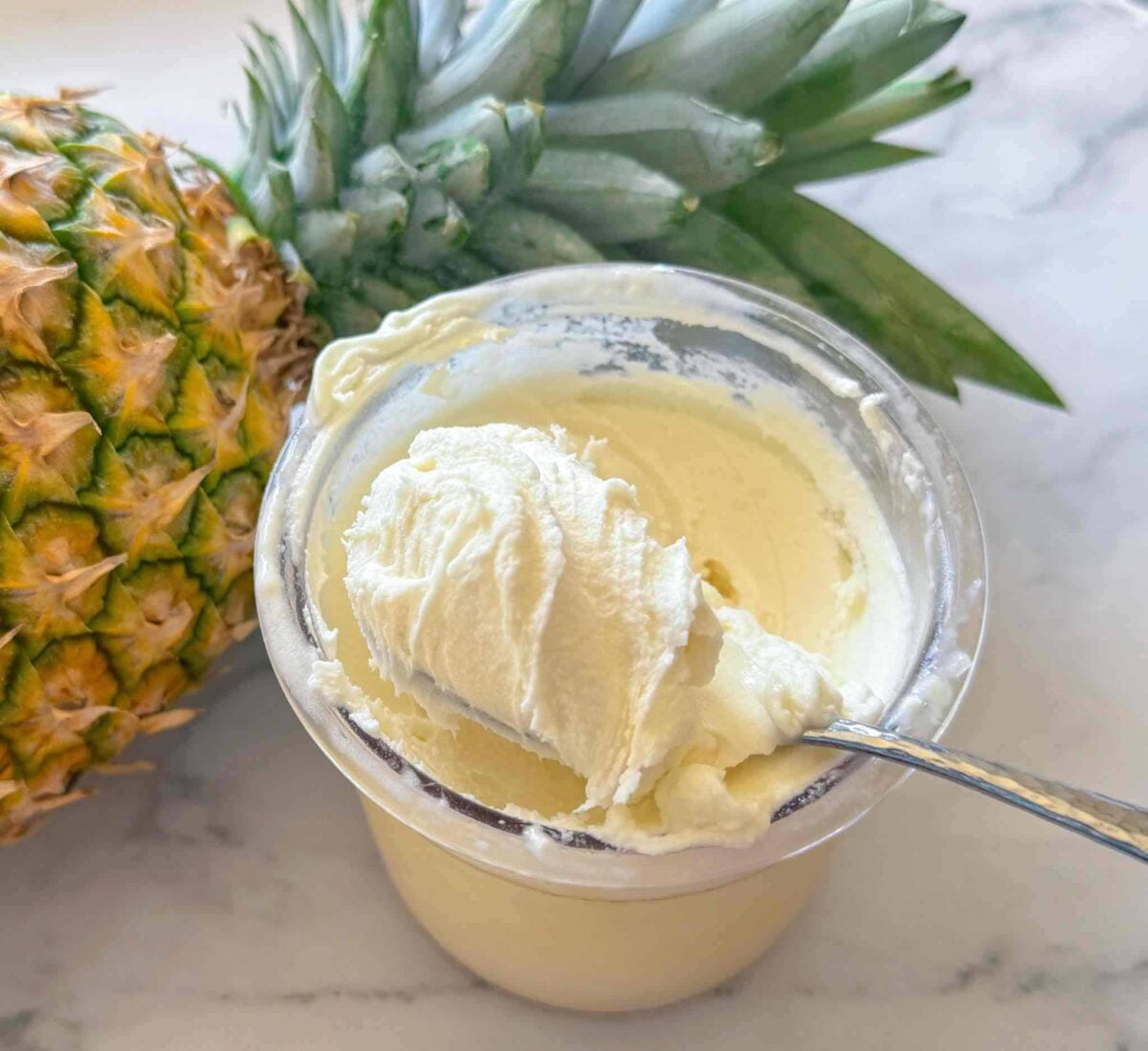 This is a ninja creami pint container with dole whip next to a pineapple with a spoon taking out a big bite.
