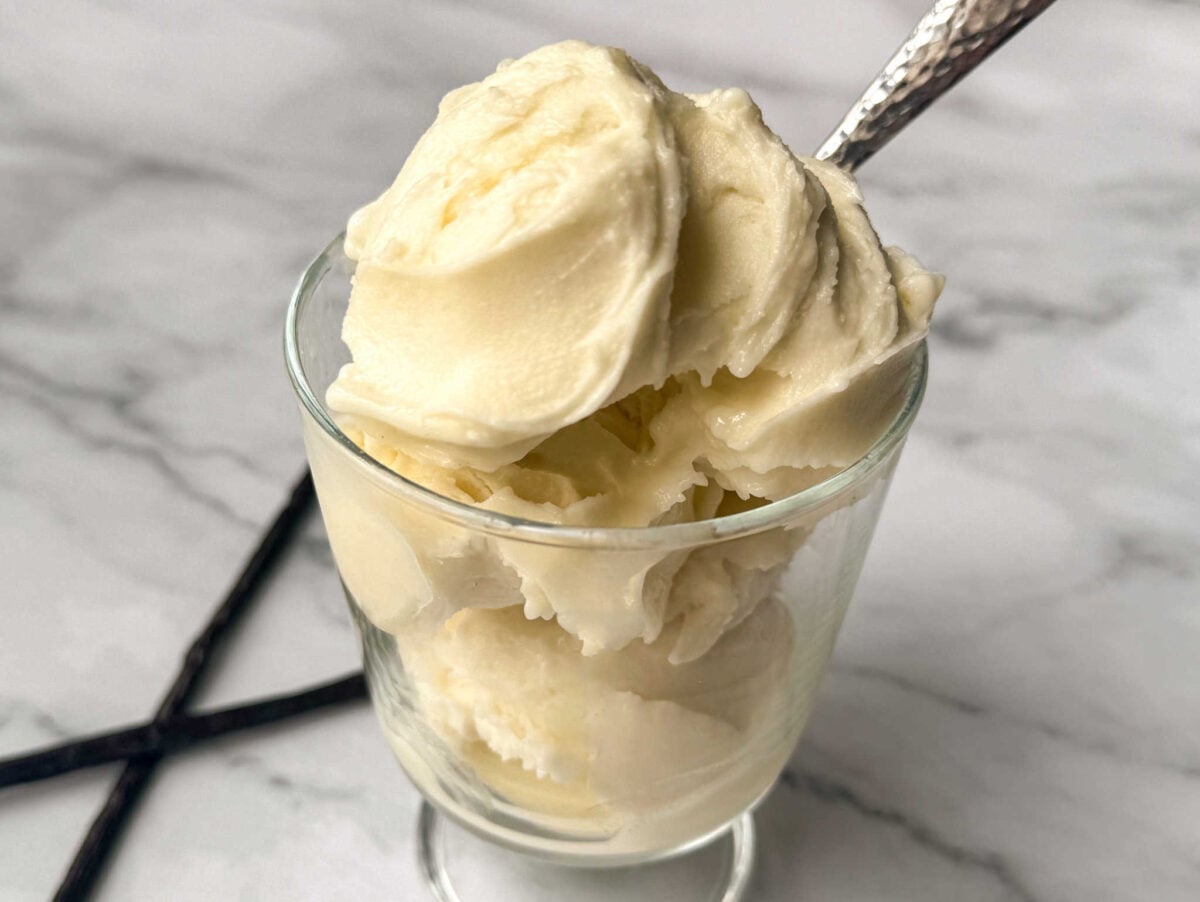 This is a glass ice cream dish with vanilla ice cream with vanilla beans in the background.