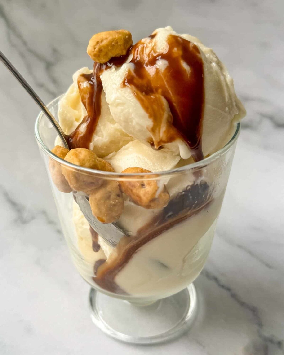 This is a vanilla Ninja Cream base recipe ice cream sundae in a glass dish with chocolate sauce and peanuts.