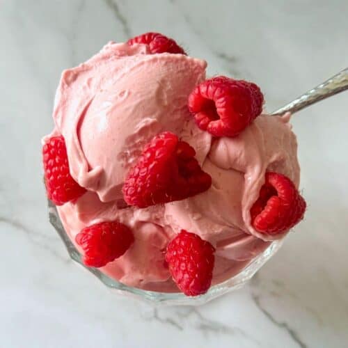 This is raspberry ice cream in a dish with fresh raspberries on top.