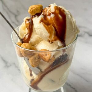 This is a vanilla Ninja Cream base recipe ice cream sundae in a glass dish with chocolate sauce and peanuts.