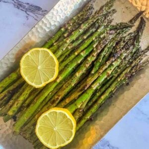 This is a silver platter of asparagus cooked on the blackstone with slices of lemon for garnish.