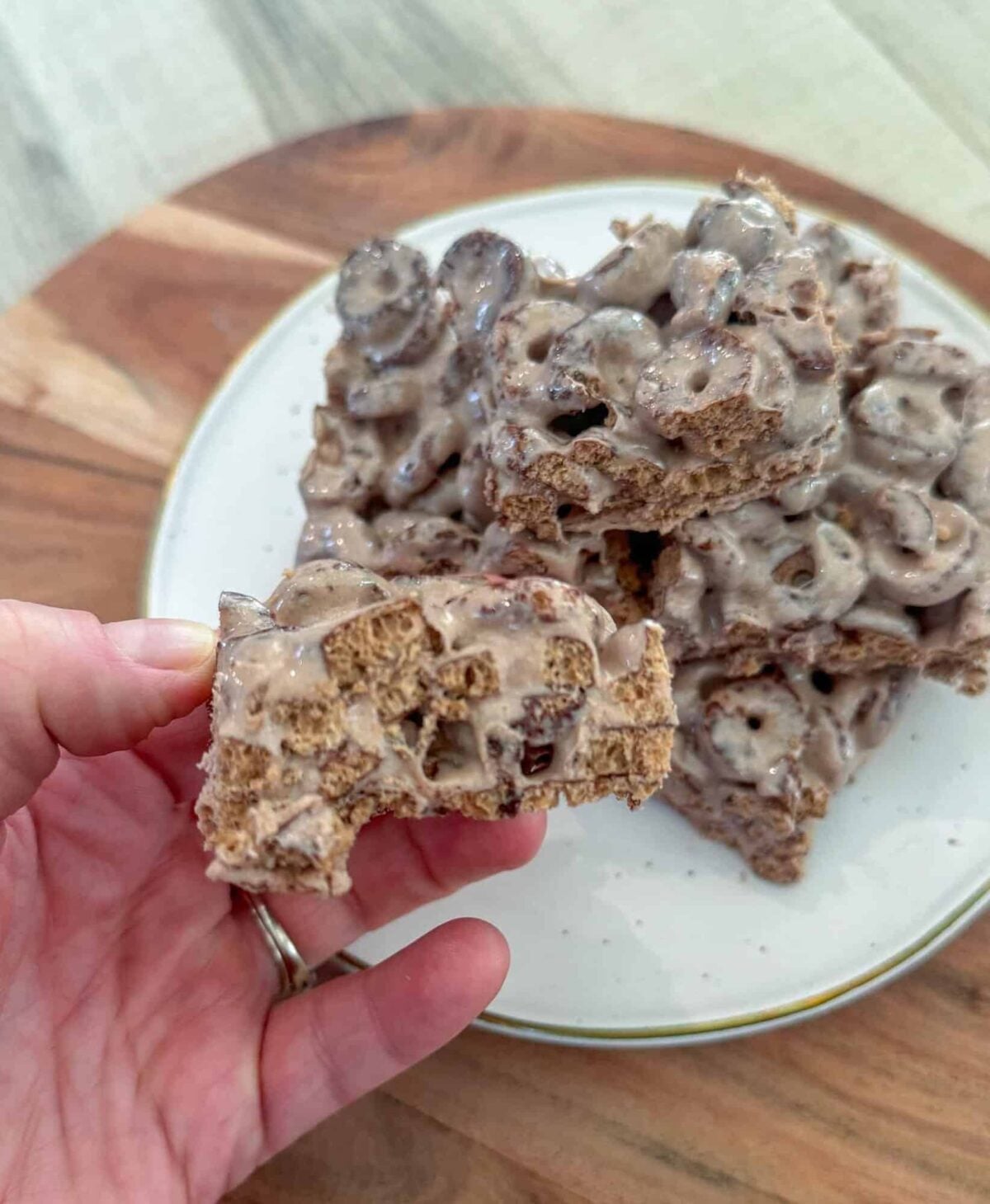 This is a stack of cereal protein bars on a white plate with a hand holding one next to it.