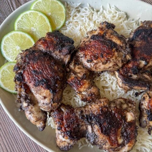 This is a plate of blackstone chicken thighs on top of coconut rice garnished with limes.