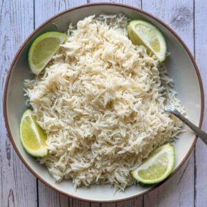 Serving bowl of coconut rice with 4 lime wedges and a silver spoon.