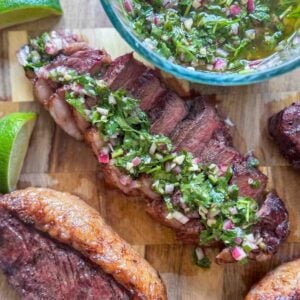 This is a sliced picanha steak topped with chimichurri on a cutting board.