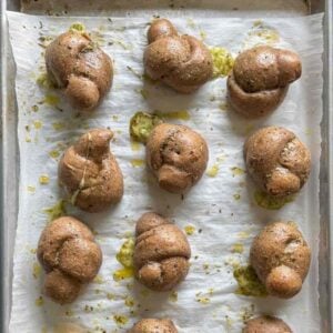 cheesy sourdough garlic knots in rows on a parchment-lined baking skeet
