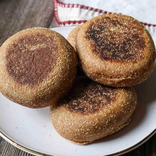A stack of pumpkin spice whole wheat sourdough english muffins on a white plate.