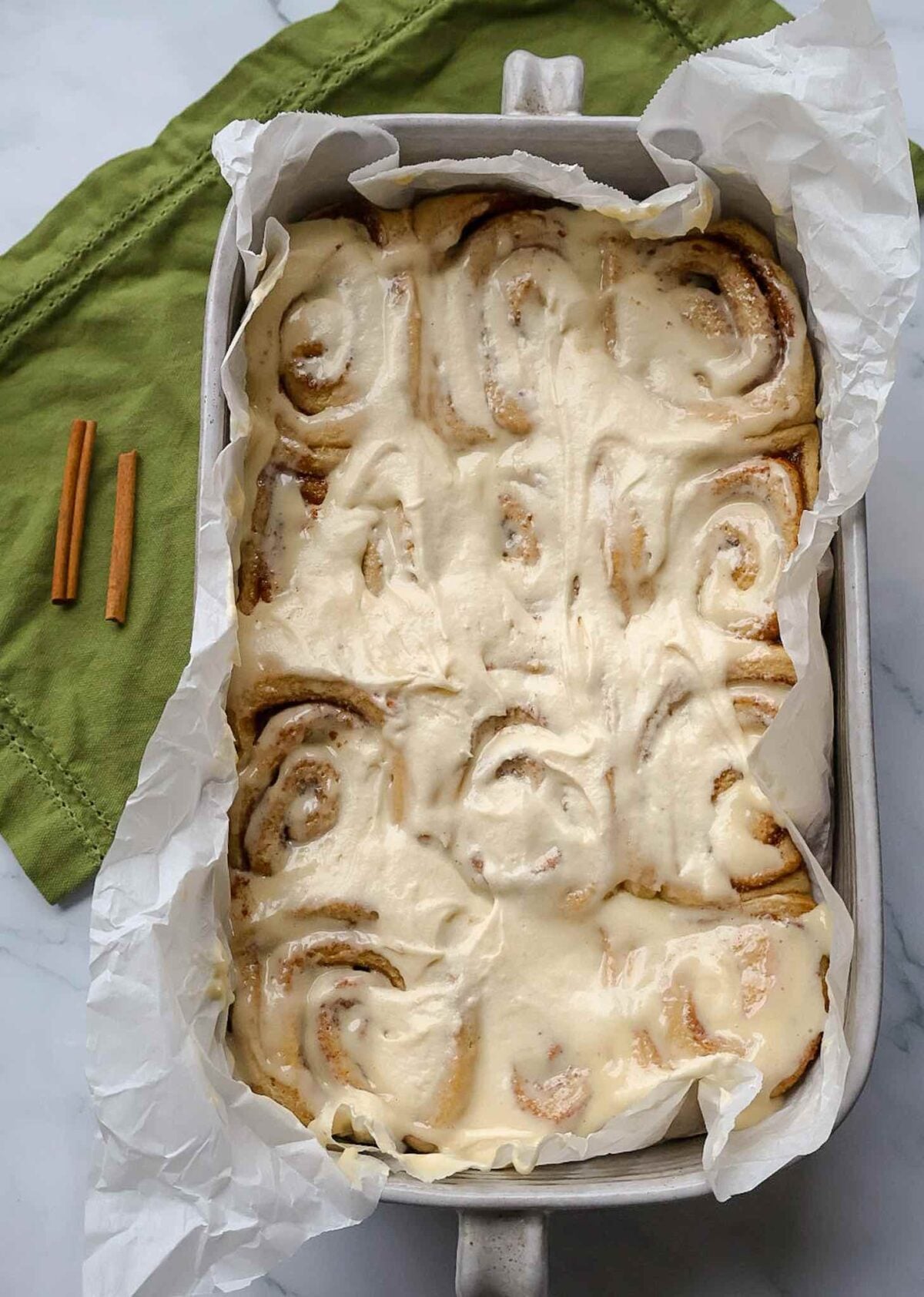 The full pan of frosted cinnamon rolls on a green napkin.