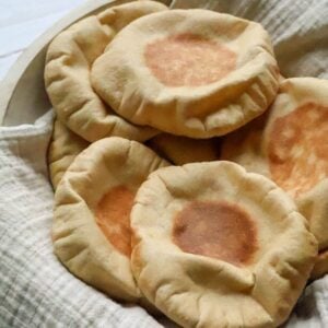 A pile of pillowy pitas on a white towel.