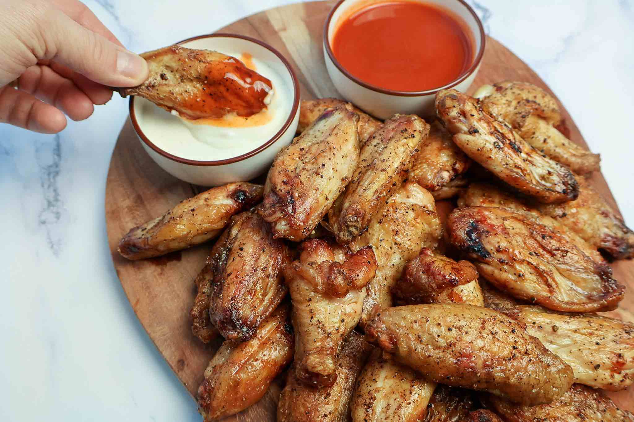 A platter of smoked wings with one being dipped in buffalo and ranch sauces.
