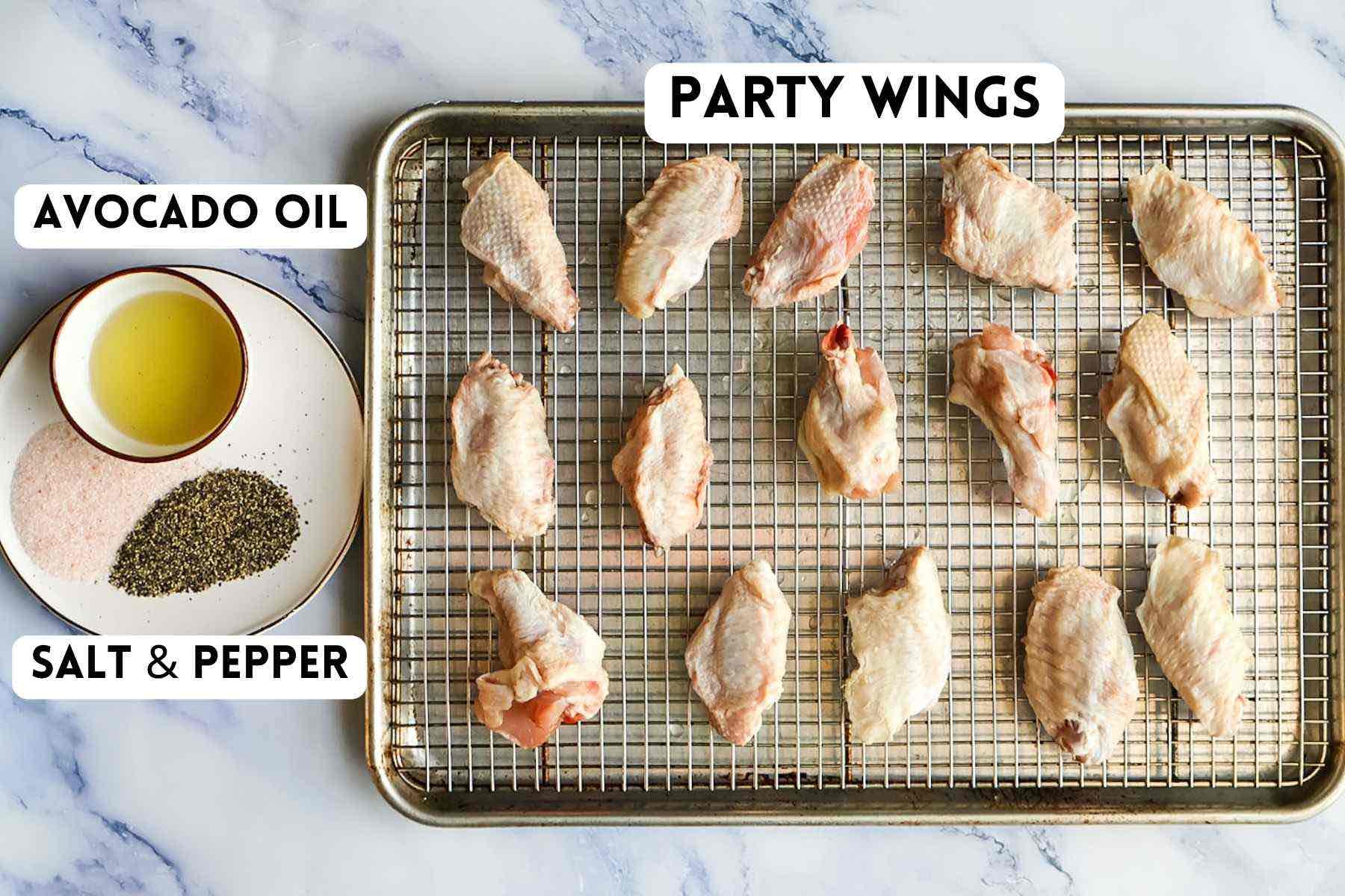 Ingredients for the smoked party wings, including raw wings on a sheet pan and a bowl of oil and plate of salt & pepper.
