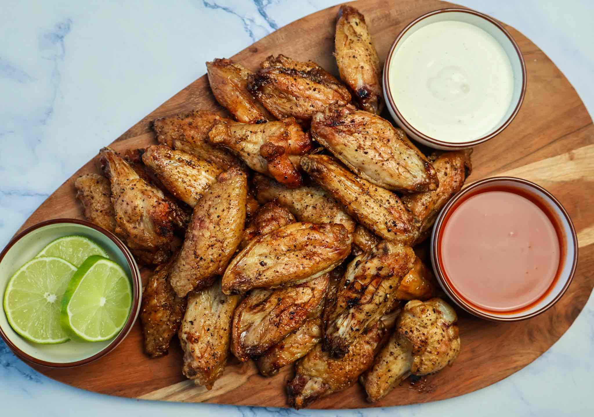 Traeger Smoked chicken wings with bowls of buffalo and ranch and a side of lime slices on a wooden serving board.
