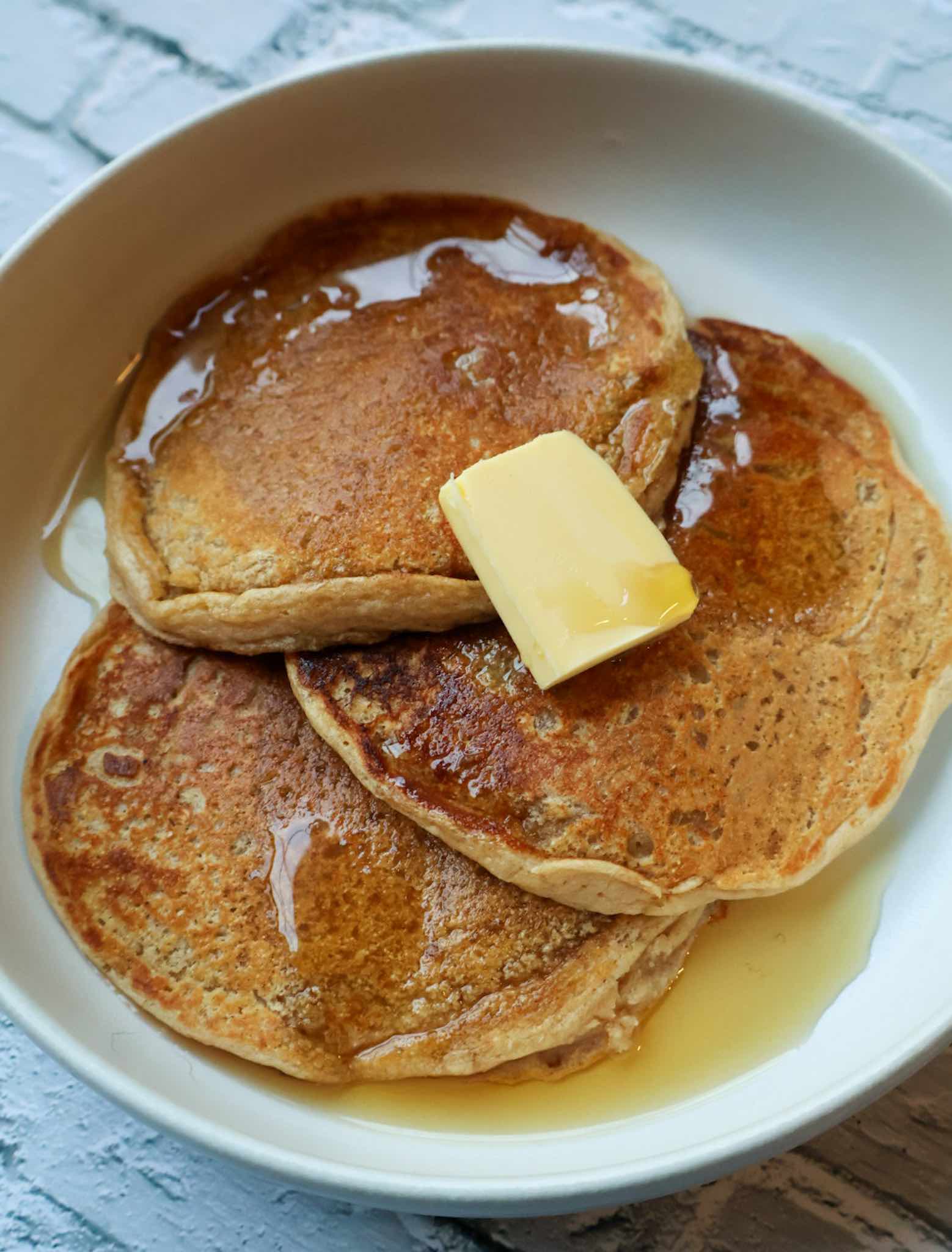 homemade protein pancakes on white plate with butter and syrup.