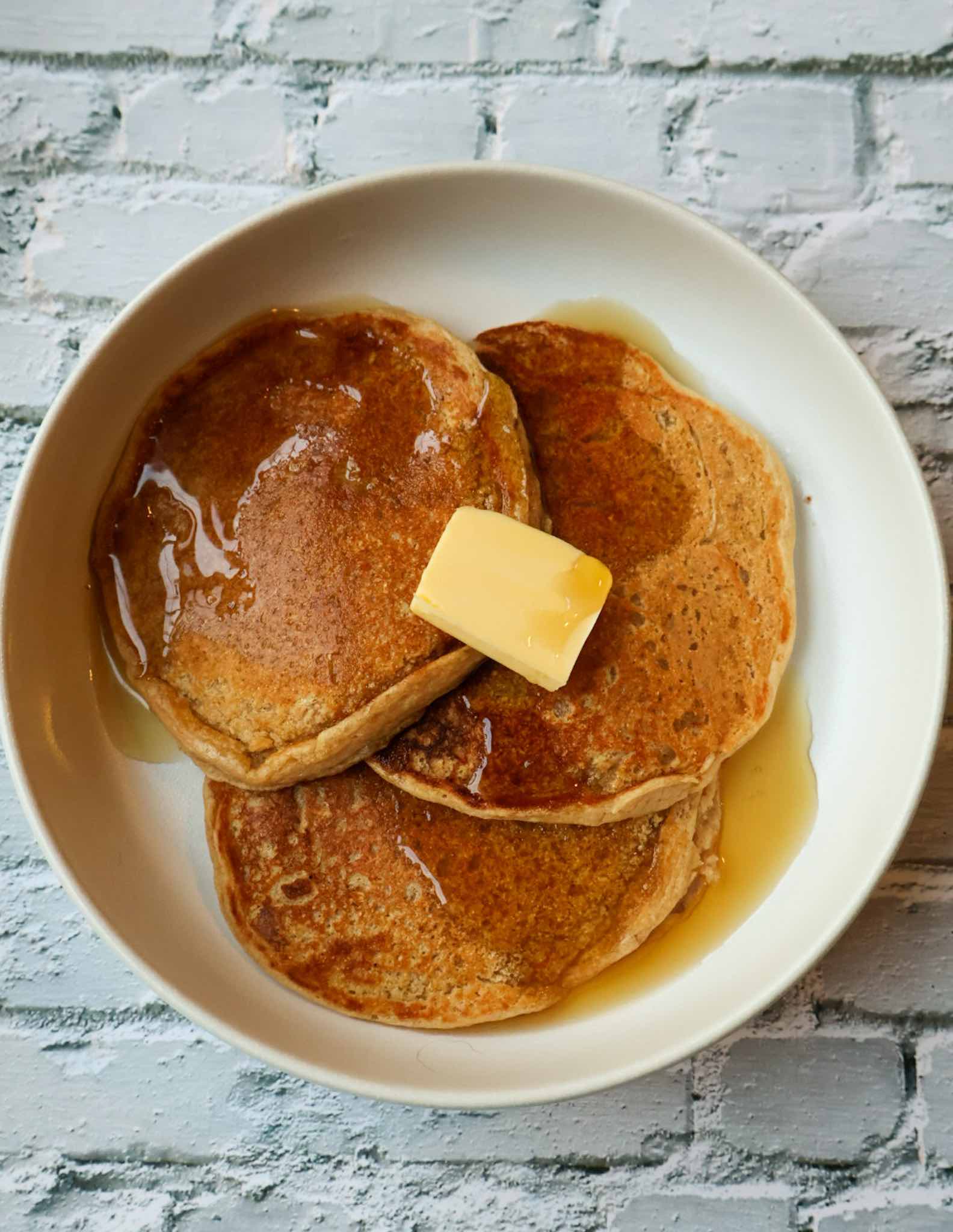 homemade protein pancakes with syrup and butter on a white plate.