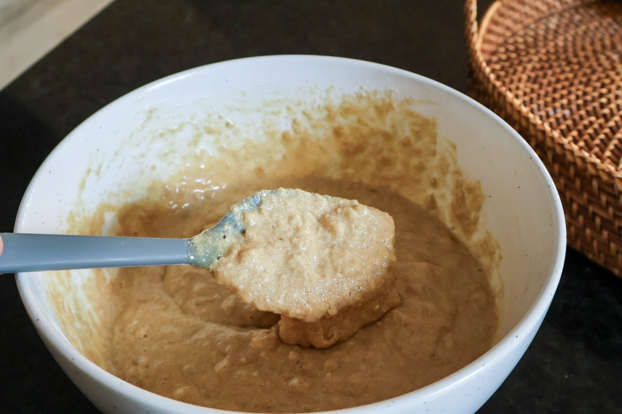 A White bowl with muffin batter and gray spatula.