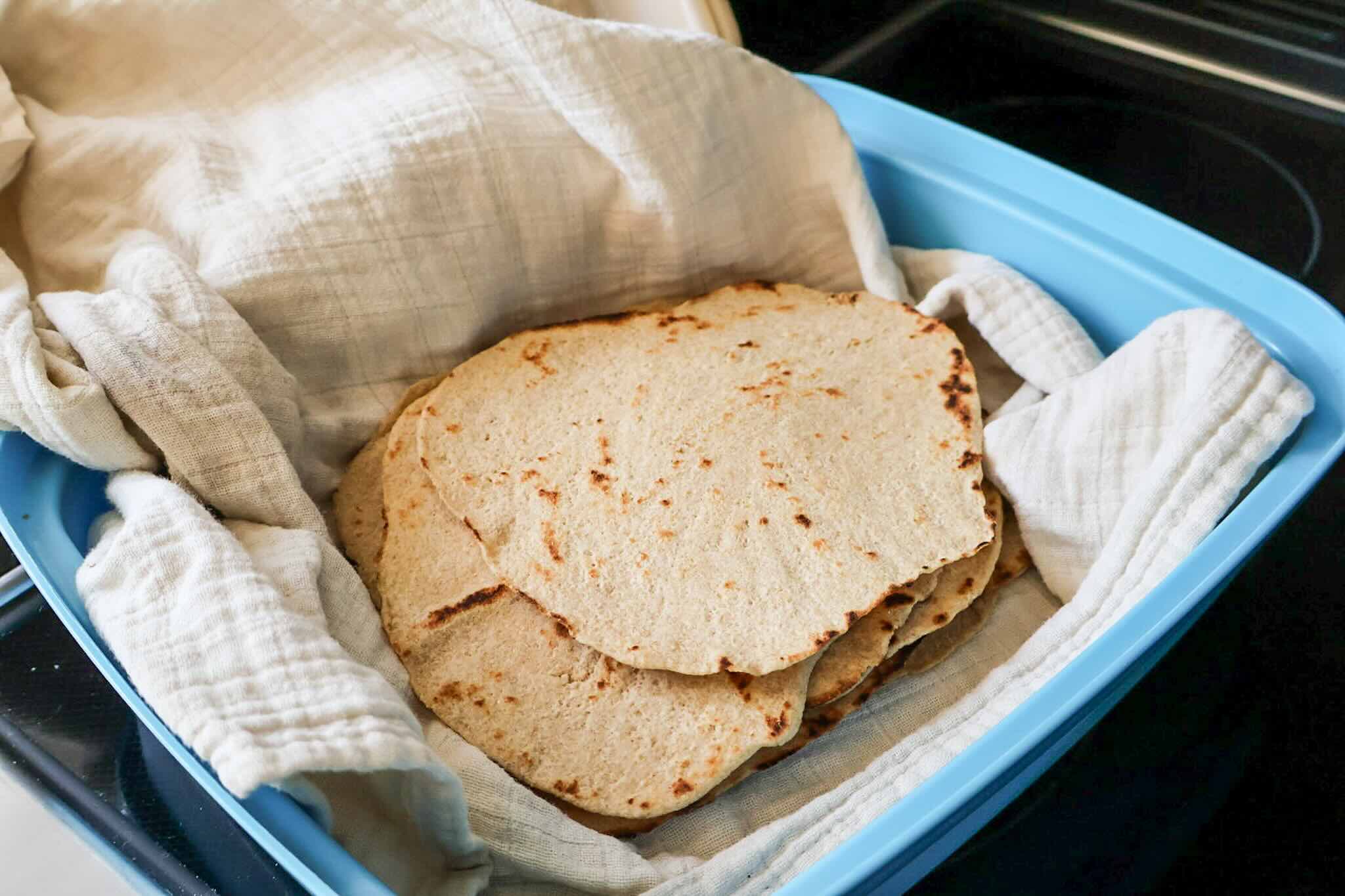 A stack of cooked tortillas in a towel in a Tupperware container.