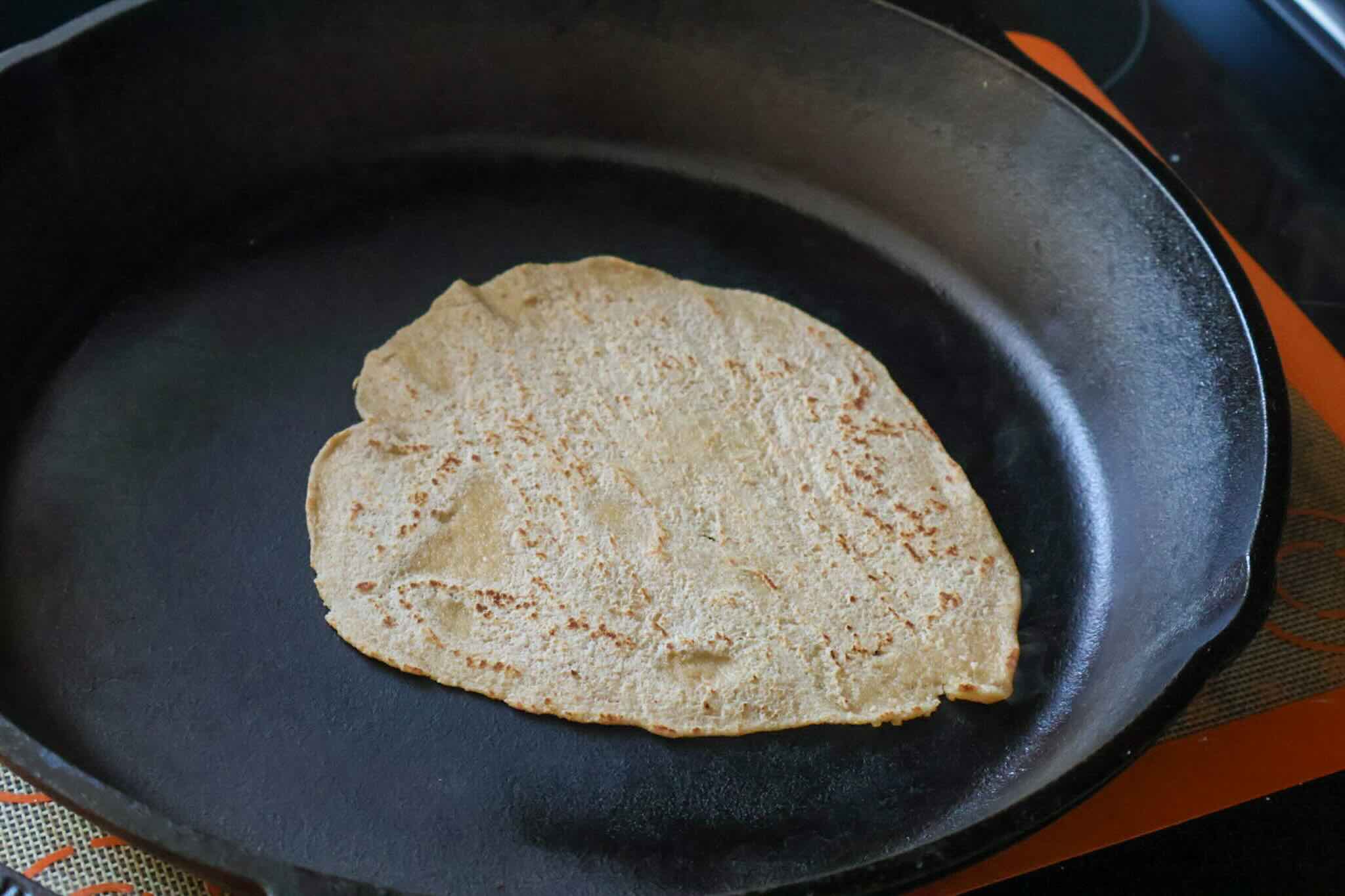 A whole wheat tortilla cooking on a cast iron skillet.