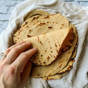 A stack of whole wheat tortillas in a towel with the top being folded to show elasticity.