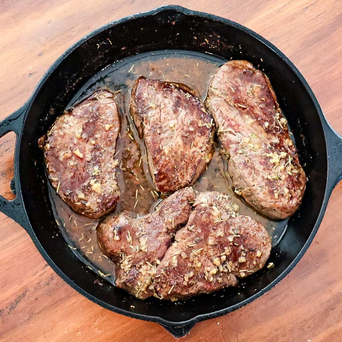 Bison tenderloin in cast iron skillet with wood background.