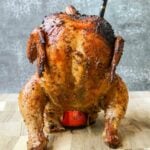 Smoked chicken on a cider can sitting on cutting board with gray background.