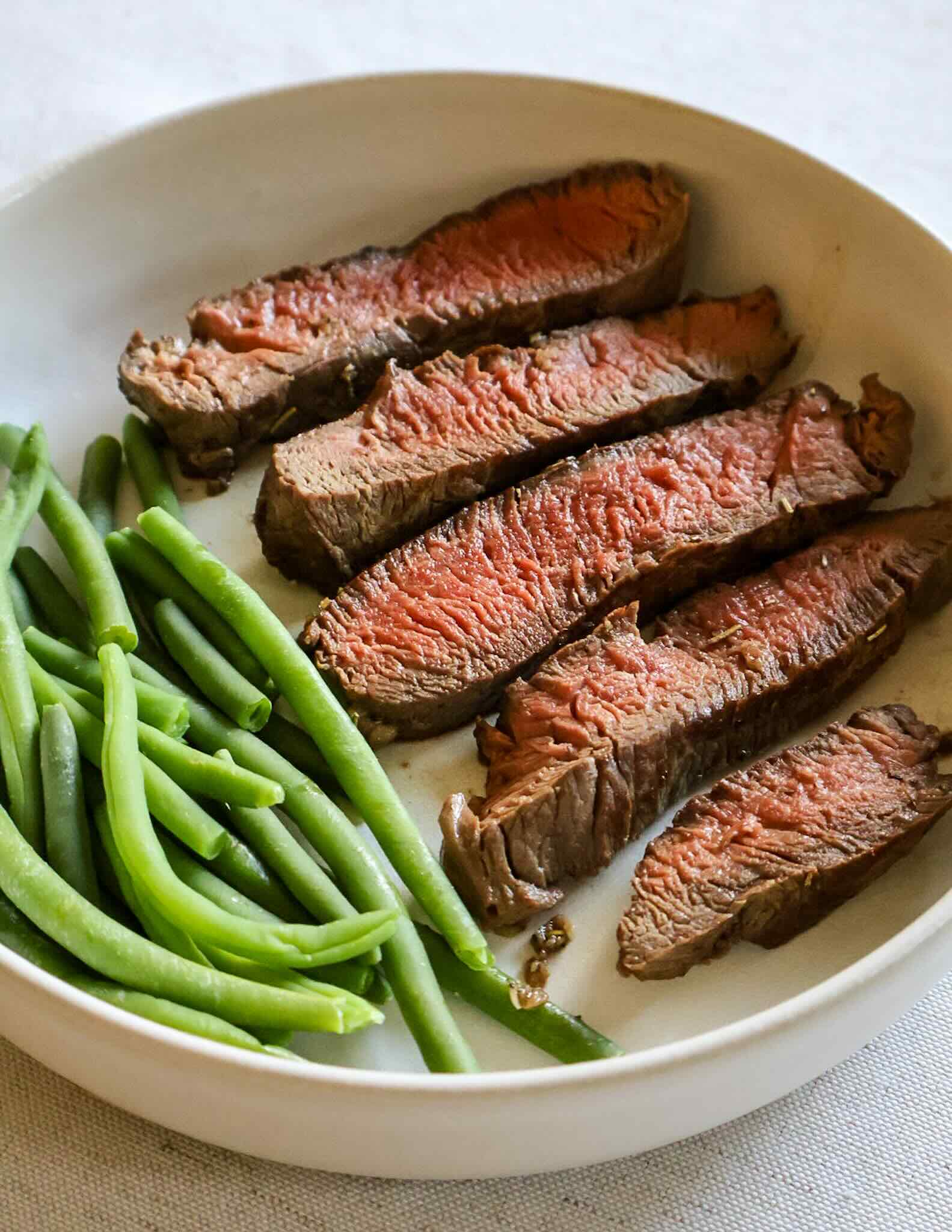 Sliced bison tenderloin with a side of green beans on white plate.