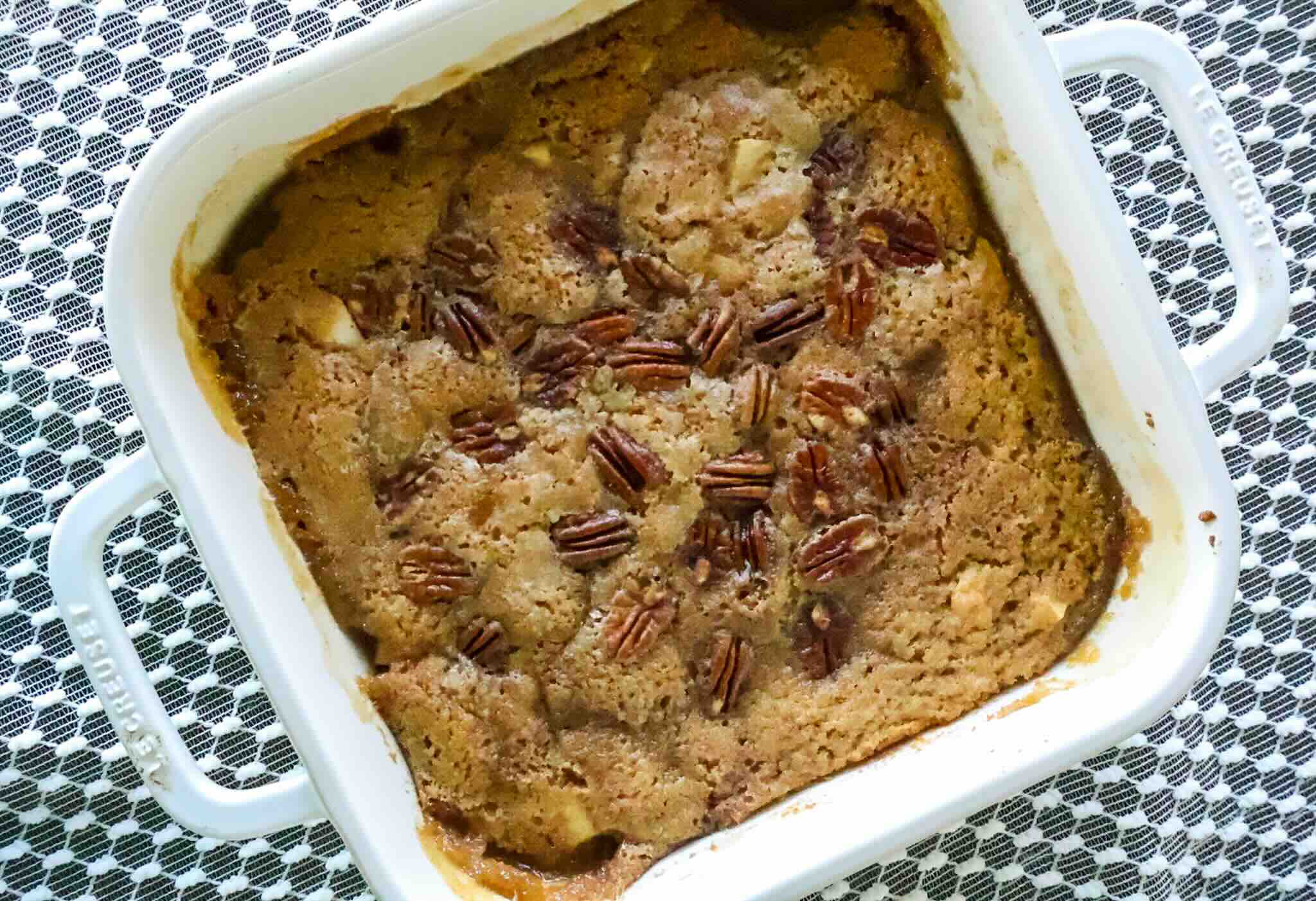 Fully baked apple cake on table with lace cloth.