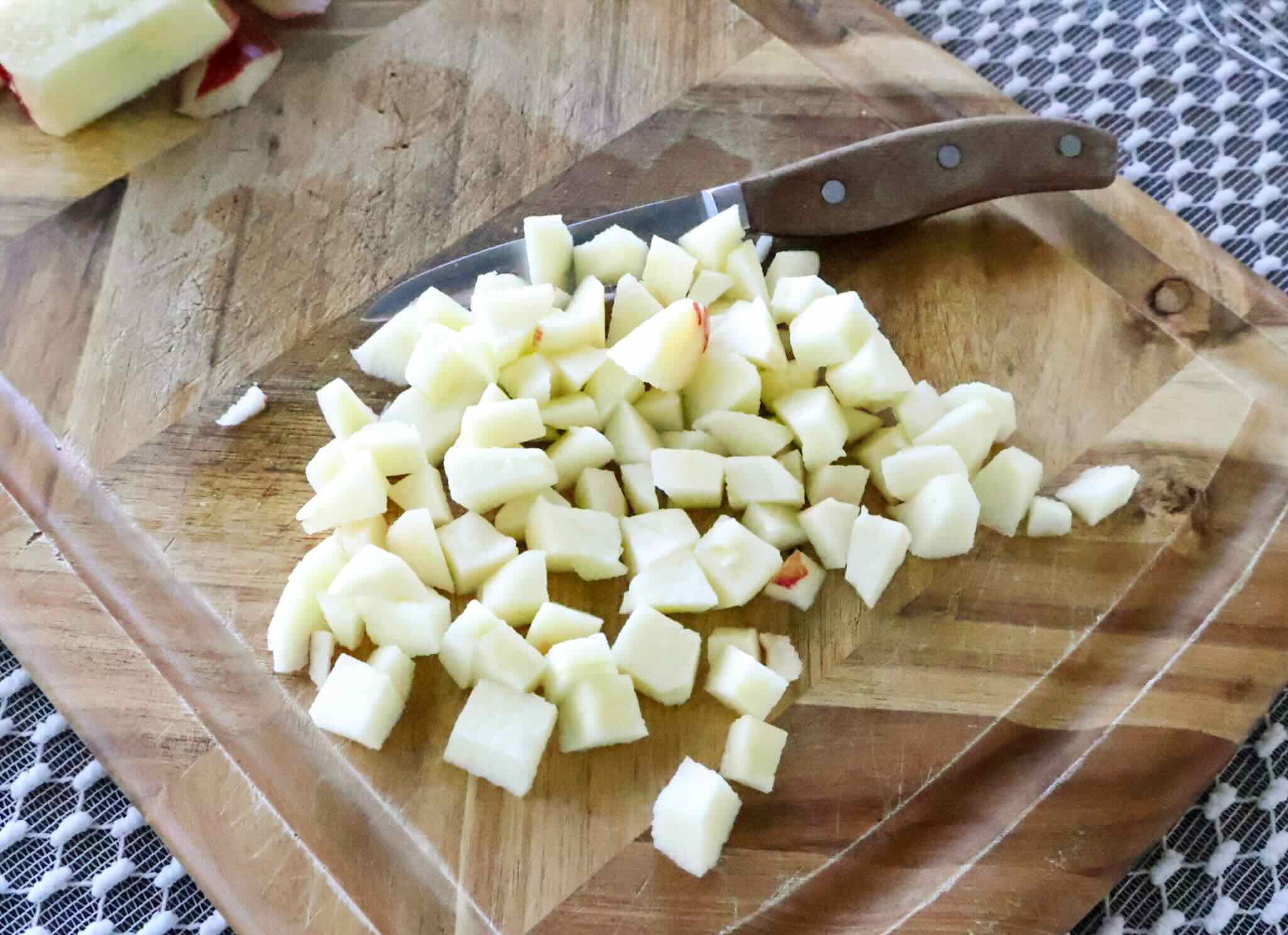 Wooden cutting board with chopped apples and knife.