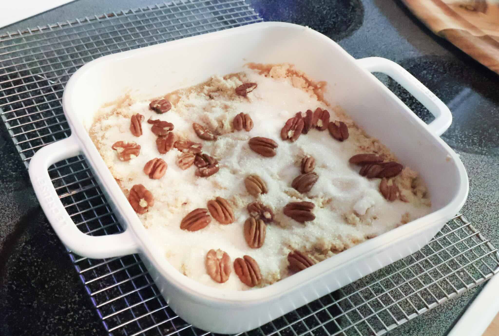 White baking dish of apple cake batter topped with sugar and nuts.