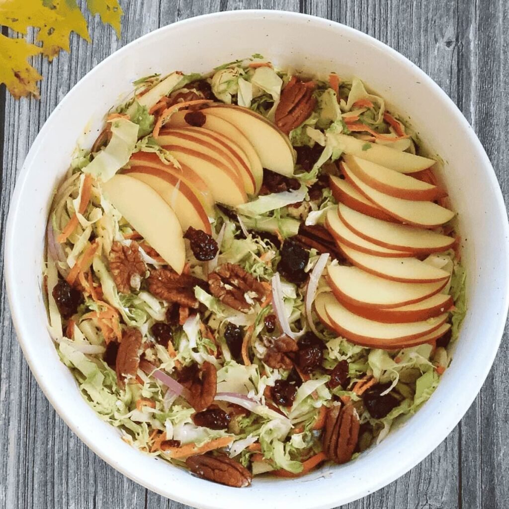 White bowl of cranberry apple coleslaw topped with apple slices for garnish.