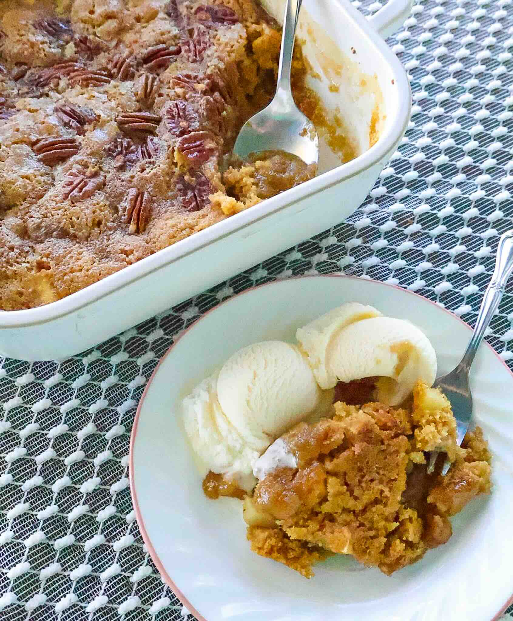 White plate with serving of apple cake and ice cream next to cake pan.