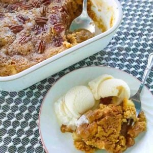 White plate of apple cake with vanilla ice cream with whole pan behind.